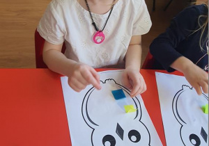Martynka nakleja piórka z papieru kolorowego.